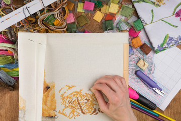 Girl sitting at a table where everything necessary for embroidery, embroiders a bigger picture © Dmitrii