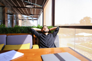 European translator sorting papers and closing laptop lid at cafe. Young persistent man dressed in...