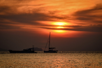 sun rises behind sailing boat with dramatic colors