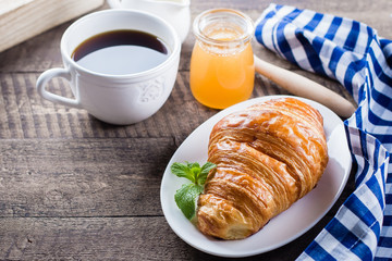 Fresh Croissant with cup of coffee, honey, milk on wooden table background. Breakfast concept. Copy space