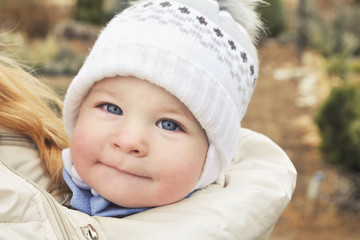 A child in a sling at the mother's under a jacket, a portrait of a baby in winter clothes