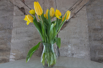 Yellow tulips and daffodils in front of the wall of an attic.