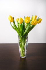 Yellow tulip in a vase on a wooden table and white wall. White copy space for a text. Top of view. Natural background. Valentines gift 