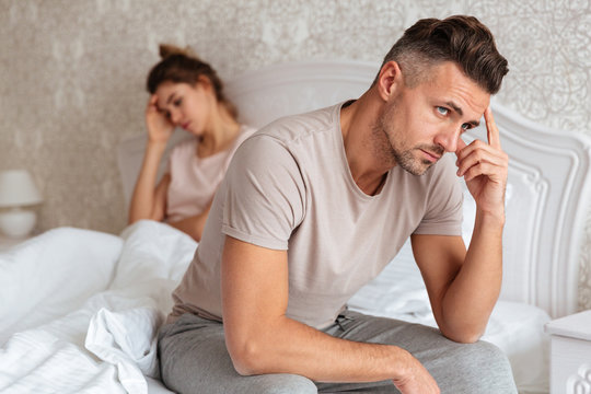 Upset pensive man sitting on bed with his girlfriend