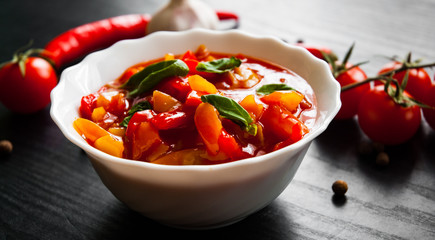 Delicious letcho with fresh vegetables in bowl on dark wooden background