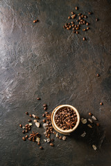 Variety of coffee beans, brown sugar, spices in wooden bowls over dark texture background. Top view, copy space