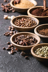 Variety of grounded, instant coffee, different coffee beans, brown sugar, spices in wooden bowls over dark texture background. Close up
