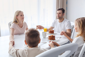Obraz na płótnie Canvas christian family praying before breakfast and holding hands