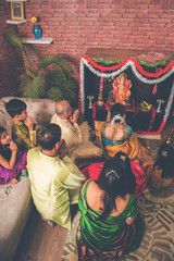 Indian  family performing Ganesh puja or Ganpati Puja in Ganesh Utsav, or holding ganesh idol over...
