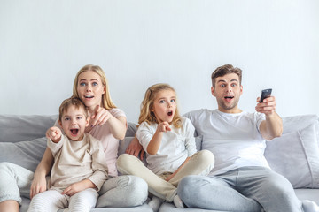 shocked young family watching movie at home and pointing at tv