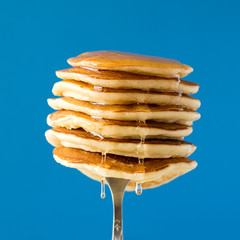 Stack of pancakes with honey decorated sweet cherry pinned on a fork on blue background - obrazy, fototapety, plakaty