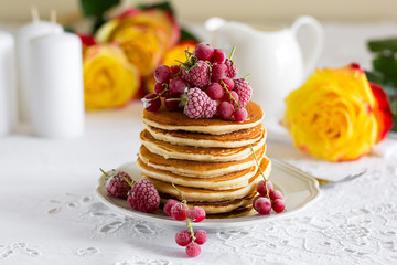 Stack of pancakes with raspberry, red currant, cream and honey on white table cloth