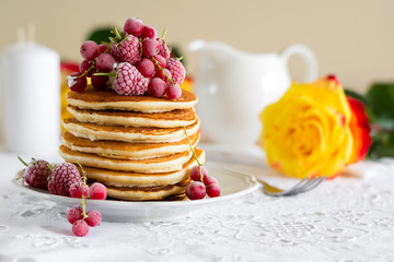 Stack of pancakes with raspberry, red currant, cream and honey on white table cloth
