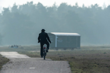 Man in hat cycling on path in misty nature reserve.