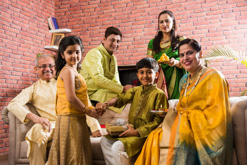 Raksha Bandhan or Rakshabandhan or Rakhi - Indian small Brother and sister celebrating Raksha Bandhan with parents and grand parents on sofa
                        