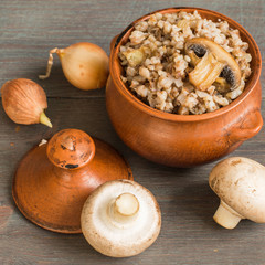 Clay pot with hot buckwheat porridge and mushrooms champignons on a gray wooden table. Vegetarian food. Lenten dishes.