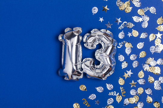 Silver foil number 13 balloon on a blue background with glitter gonfetti