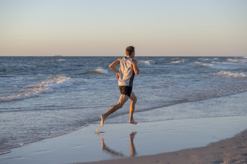 athletic fit and strong runner man training on Summer sunset beach in sea shore running and fitness workout in sport and healthy lifestyle