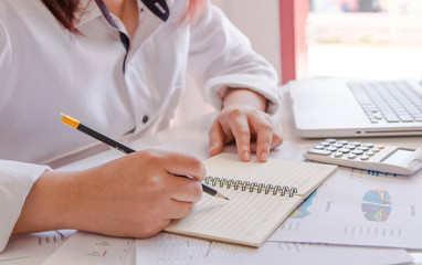 Close up woman hand using calculator and writing make note with calculate about cost at home office.