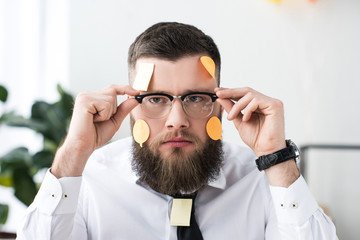 portrait of businessman in eyeglasses with sticky notes on face in office