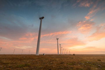 Fototapeta premium Wind turbines against red, blue and orange sunrise