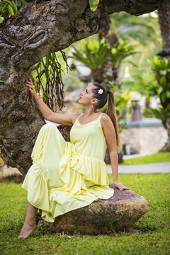 girl in yellow dress seats on the tree roots in garden