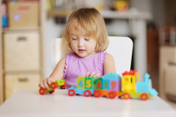 Little blond girl  playing with  colorful plastic blocks indoor.