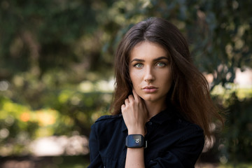 Fototapeta premium Portrait of a beautiful girl on the street with a hand with a clock at the face. Smart watch..