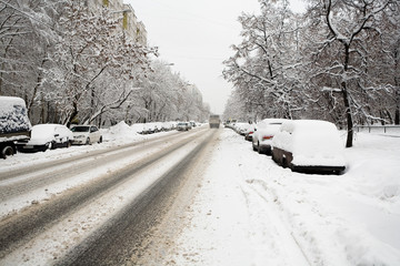 The road and the parked cars are covered with snow.