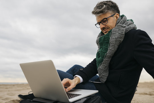 Businessman sitting on the beach in winter using laptop