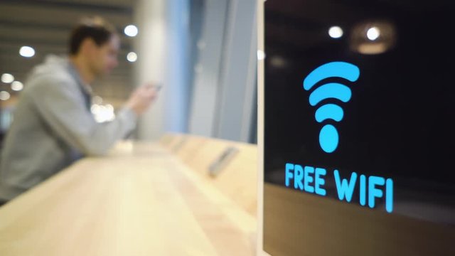 young man uses a phone on a background of a Free Wifi Signal Sign flashes on display in a cafe