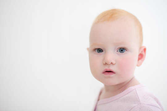 Baby girl in pink body looks at the camera on the white background