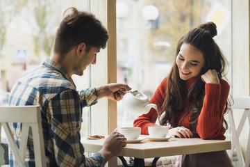 A guy and a girl are sitting together in a cafe. They drink tea. They are in love with each other. They are a couple.