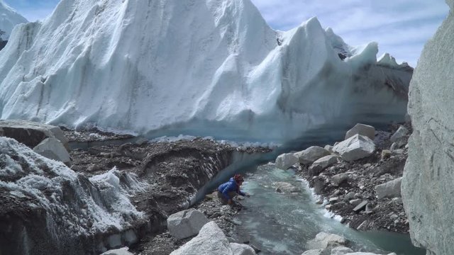 The Khumbu Glacier descends from Mount Everest. Walking on the glacier is very dangerous. A girl drinks water from a creek. Nepal. Himalayas. 4K