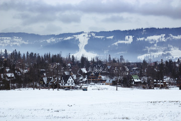 Fototapeta premium Panorama at the little tourist village in the winter, in the background forest, mountain and ski slope with ski lifts