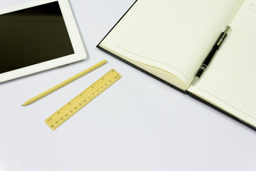 Office table with tablet, pen, notebook on white background.