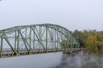Iron bridge crosses a smoke and fog covered river in vermont