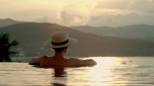 Woman enjoying bathing in luxury infinity pool on background evening sunset