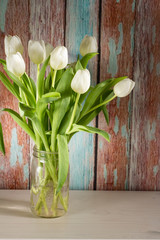 White tulips in glass jar. Wooden background.