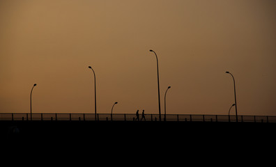 People walking on the bridge at sunset ...