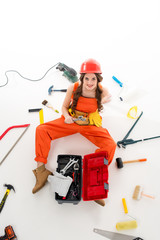 overhead view of girl in overalls sitting on floor with toolbox and different equipment, isolated on white