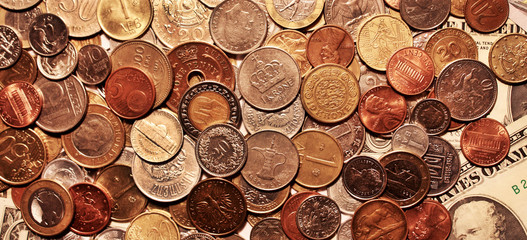 Background of coins lying on banknotes of United States. Currencies of different countries. Backdrop of scattering metal cash on dollars. Huge pile of coins on paper money. Horizontal location.