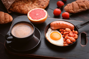 English breakfast. sausage, fried eggs and beans in tomato. coffee and bread nearby.