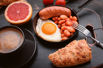 English breakfast. sausage, fried eggs and beans in tomato. coffee and bread nearby.