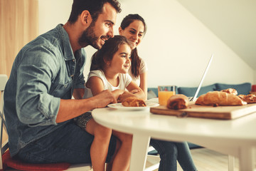 Family breakfast.Young parents with they daughter sitting at the table and watching cartoons on laptop. © BalanceFormCreative