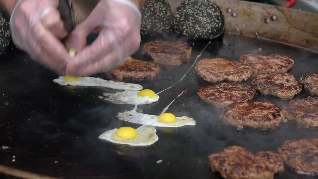 Cutlets for black burger and eggs are fried in a large frying pan outdoors.