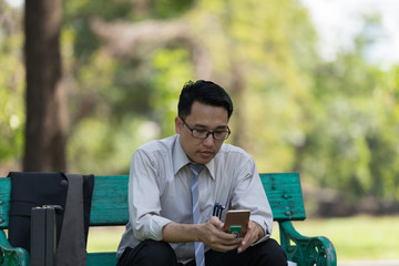 Fototapeta premium Business man sit check email on mobile phone at the Park on the way back home.