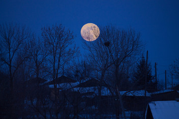 the full moon rising over a country house in winter