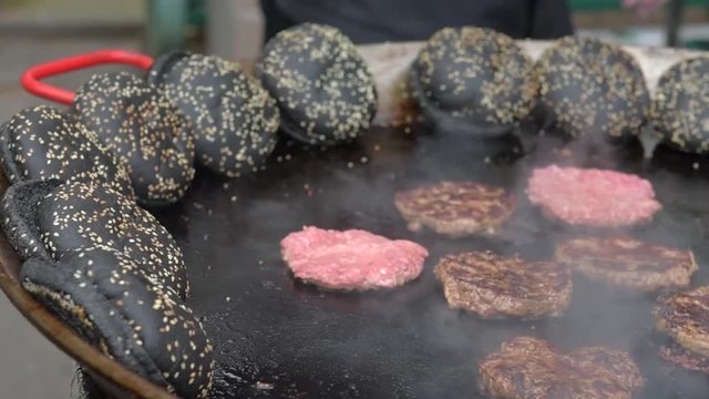 Cutlets for black burger  are fried in a large frying pan outdoors.