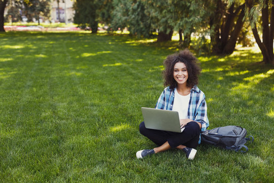 Cheerful young woman using laptop in park